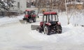 Two different small red tractor snow plows during work