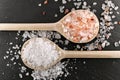 two different types of coarse salt on wooden cooking spoons on black slate background, top view