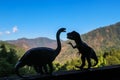 Two dinosaurs - a brontosaurus and a t rex -  confront each other in silhouette with out of focus mountains in the distance Royalty Free Stock Photo