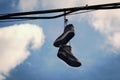 Two dirty old sneakers hanging on wires in blue sky with clouds Royalty Free Stock Photo