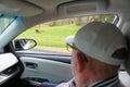 Two distant horses graze while elderly man looks on from car