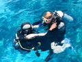 Two divers in black scuba diving suits, a man and a woman with oxygen bottles sink under the transparent blue water in the sea, th