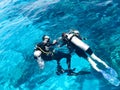 Two divers in black scuba diving suits, a man and a woman with oxygen bottles sink under the transparent blue water in the sea, th Royalty Free Stock Photo