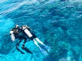 Two divers in black scuba diving suits, a man and a woman with oxygen bottles sink under the transparent blue water in the sea, th Royalty Free Stock Photo