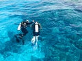 Two divers in black scuba diving suits, a man and a woman with oxygen bottles sink under the transparent blue water in the sea, th Royalty Free Stock Photo