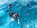 Two divers in black scuba diving suits, a man and a woman with oxygen bottles sink under the transparent blue water in the sea, th