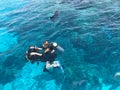 Two divers in black scuba diving suits, a man and a woman with oxygen bottles sink under the transparent blue water in the sea, th Royalty Free Stock Photo