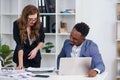 Two diverse businesspeople chatting sitting behind laptop in office. Excited caucasian female sharing ideas or startup Royalty Free Stock Photo