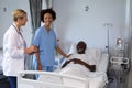 Two diverse female doctors and african american male patient in hospital room smiling to each other Royalty Free Stock Photo