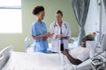 Two diverse female doctors and african american male patient in hospital room talking Royalty Free Stock Photo