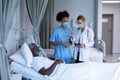 Two diverse female doctors talking to african american male in hospital patient room Royalty Free Stock Photo