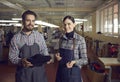 Two diverse shoemaker in uniform smiling posing for camera with handmade boot
