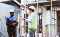 Two diversity male engineers team working, inspecting outdoor at construction site, wearing hard hats for safety, talking, Royalty Free Stock Photo