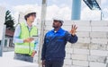 Two diversity male engineers team working, inspecting outdoor at construction site, wearing hard hats for safety, talking, Royalty Free Stock Photo