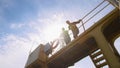 Two dockers, coworkers and colleages look at the camera and hand waving at an industrial harbor