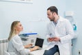 Two doctors colleagues are sitting at the work place and using modern technology for their work, in white coats, focused Royalty Free Stock Photo