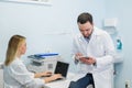 Two doctors colleagues are sitting at the work place and using modern technology for their work, in white coats, focused Royalty Free Stock Photo