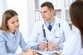 Two doctors and patient sitting at the table in medical cabinet.