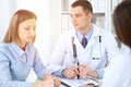 Two doctors and patient sitting at the table in medical cabinet.