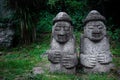 Two Dol Hareubang statues in dark green forest, Seogwipo, Jeju Island, South Korea Royalty Free Stock Photo