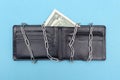 Two dollars are in the wallet. Leather wallet blocked by chains for savings, business concept. Blue background. Bankrupt