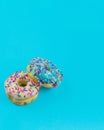 Two donuts with icing and sprinkles on a plain blue background with copy space