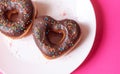 two donuts in a heartshape on a white plate and on a pink background. Concept for Valentine's Day. Valentine's Royalty Free Stock Photo