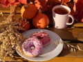 Two donuts with pink icing are on a plate. Nearby lies a bouquet of vines,