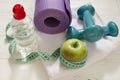 Two dumbbells, bottle of water, green apple, centimeter on white