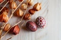 two Easter eggs in brown colors and physalis branches on a wooden surface