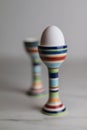 Two eggcups on a marble table with colorful stripes and only one