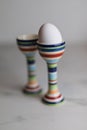 Two eggcups on a marble table with colorful stripes and only one