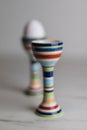 Two eggcups on a marble table with colorful stripes and only one