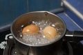 Two eggs in boiling water in stainless steel pan on the kitchen stove Royalty Free Stock Photo