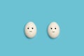 Two eggs with happy and angry face shape on a blue background Royalty Free Stock Photo