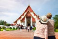 Two elderly Asian tourists Wearing a hat taking pictures of a Thai temple