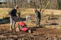 Two elderly men tilling ground soil with a rototiller in the garden.