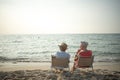 Two elderly men and women sit chair at the beach talking and watching the sun and the sea on their summer vacation and they smile Royalty Free Stock Photo