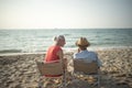 Two elderly men and women sit chair at the beach talking and watching the sun and the sea on their summer vacation and they smile Royalty Free Stock Photo