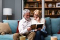 Two elderly people senior couple man and woman looking at a family photo smile and hug while sitting at home on sofa. memories and Royalty Free Stock Photo