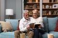 Two elderly people senior couple man and woman looking at a family photo smile and hug while sitting at home on sofa. memories and Royalty Free Stock Photo