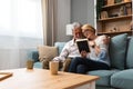 Two elderly people senior couple man and woman looking at a family photo smile and hug while sitting at home on sofa. memories and Royalty Free Stock Photo