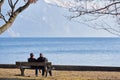 Two elderly people sit on a bench and look at the lake Traunsee. The lake is located near the city of Gmunden