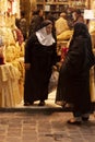 Two elderly Syrian women wearing black hijab are standing in front of a boutique shop