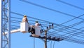 Two electricians on bucket boom truck are installing electrical system on power pole against blue clear sky background Royalty Free Stock Photo