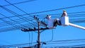 Two electricians on electric cable car are working to install power line against blue clear sky background in sunny day Royalty Free Stock Photo