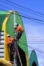 Two electricians installing electric cable lines on power pole near colorful warehouse building against blue sky background Royalty Free Stock Photo