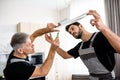 Two electricians, workers in uniform installing electric lamp, light inside apartment in the kitchen. Construction