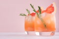 Two elegance cold wet drinking glasses with fresh grapefruit summer alcohol cocktail, ice, rosemary on fashion pink background. Royalty Free Stock Photo