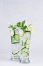 Two elegance glasses with cold detox water with slices cucumber, lime, mint, ice, straw on white wood plank, closeup. Royalty Free Stock Photo